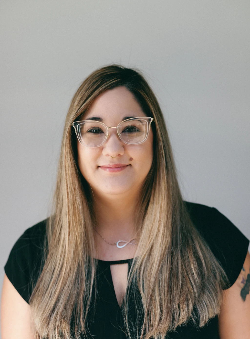 A woman wearing glasses and a black top smiles confidently, showcasing her dental hygiene.